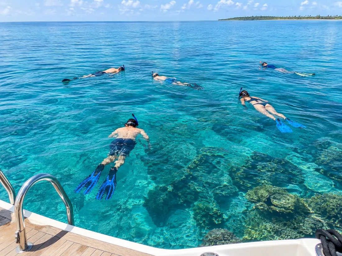 Snorkelers floating face down on calm, clear turquoise water seen from a boat